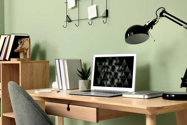绿色墙壁附近木制书桌上的现代笔记本电脑 灯和文具 总部办公室 — 图库照片