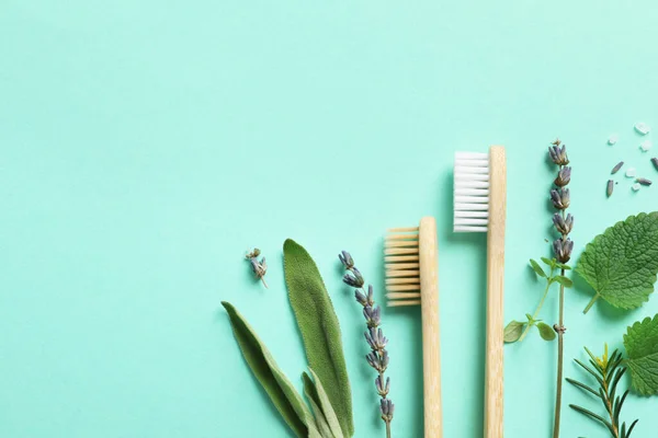 Flat lay composition with bamboo toothbrushes and herbs on turquoise background. Space for text