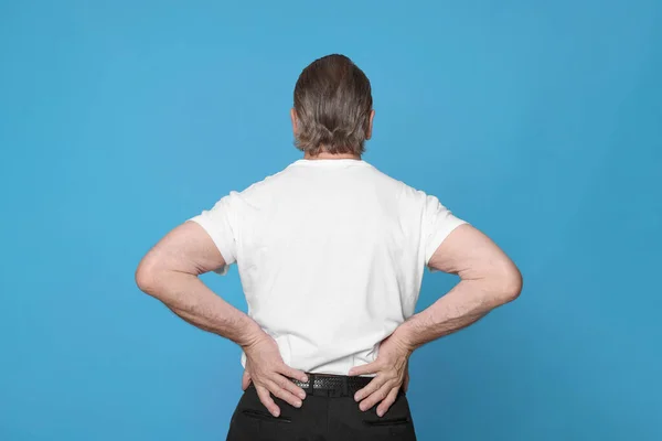 薄い青の背景で背中の痛みに苦しんでいるシニア男 関節炎の症状 — ストック写真