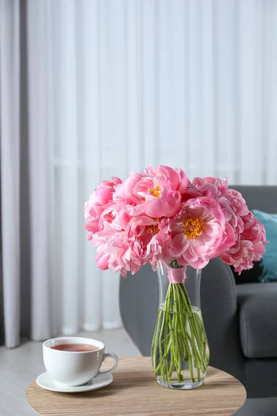花瓶にピンク色の牡丹の美しい花束と木製のテーブルの上で飲むカップ屋内 — ストック写真