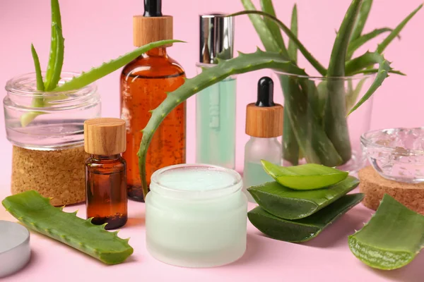 Cosmetic products and cut aloe on pink background