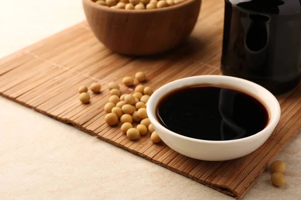 stock image Soy sauce in bowl and soybeans on bamboo mat, closeup