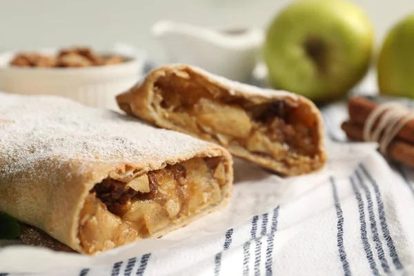 Delicious strudel with apples, nuts and powdered sugar on table, closeup. Space for text