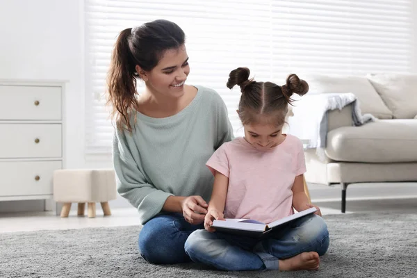年轻的母亲和她的女儿在家里的地板上看书 — 图库照片