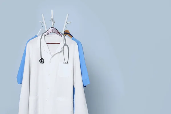 stock image Medical uniforms and stethoscope hanging on rack against light grey background. Space for text