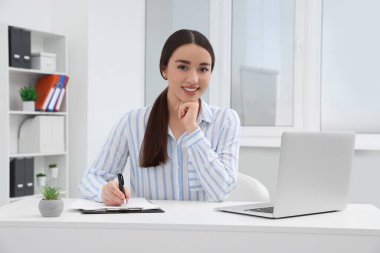 Ofiste dizüstü bilgisayarla çalışan genç bir kadın stajyer.