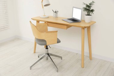 Rahat koltuk, masa, dizüstü bilgisayar ve lambayla şık bir ofis.
