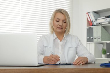 Klinikteki tahta masada dizüstü bilgisayarı ve panosu olan bir doktor.