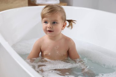 Şirin küçük kız evde köpüklü banyo yapıyor.
