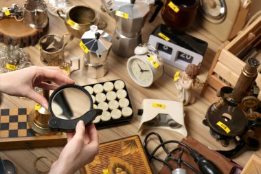 Masanın yanında elinde büyüteçle farklı şeyler tutan bir kadın. Garaj satışı