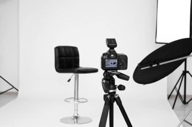 Camera on tripod, bar stool and professional lighting equipment in modern photo studio, space for text