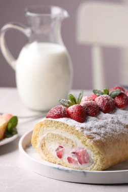 Çilekli kek rulosu ve açık gri masada krema.