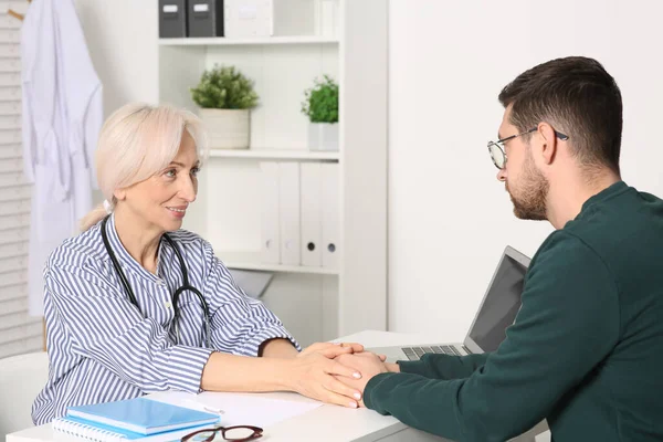 Klinikteki muayene sırasında beyaz masada hastanın elini tutan doktor.