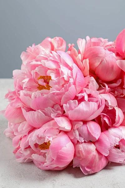 Beautiful pink peonies on white table against grey background, closeup
