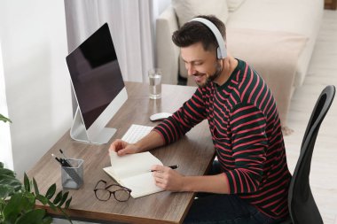 Kulaklıklı adam evde bilgisayar başında çalışıyor. Çevrimiçi çeviri kursu