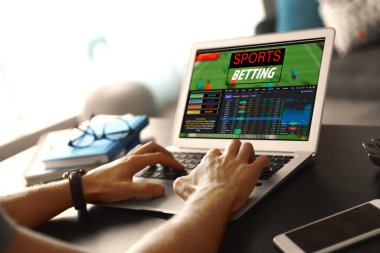 Masada dizüstü bilgisayarla spor bahisleri oynayan adam, yakın plan. Bahisçinin web sitesi ekranda