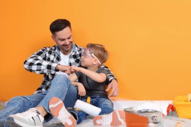 Turuncu duvarın yanında tamir aletleri olan baba ve oğul, metin için boşluk.