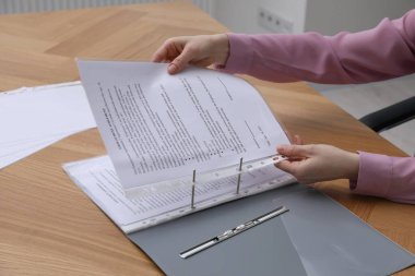 Woman putting punched pocket with document into folder at wooden table, closeup clipart