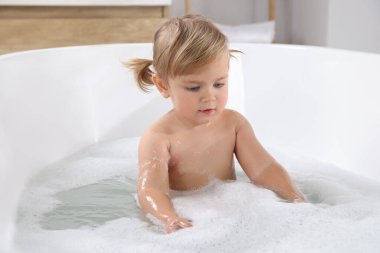 Şirin küçük kız evde köpüklü banyo yapıyor.