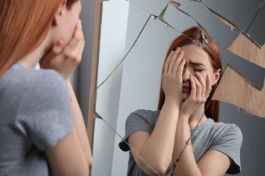 Kırık aynanın yanında ruhsal sorunları olan duygusal genç bir kadın.