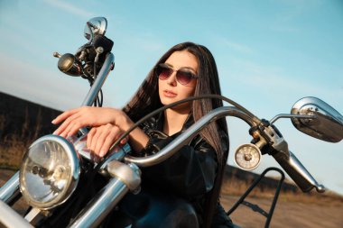Beautiful young woman sitting on motorcycle outdoors