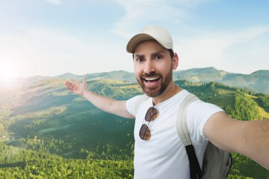 Gülümseyen adam güneşli bir sabahta dağlarda selfie çekiyor.