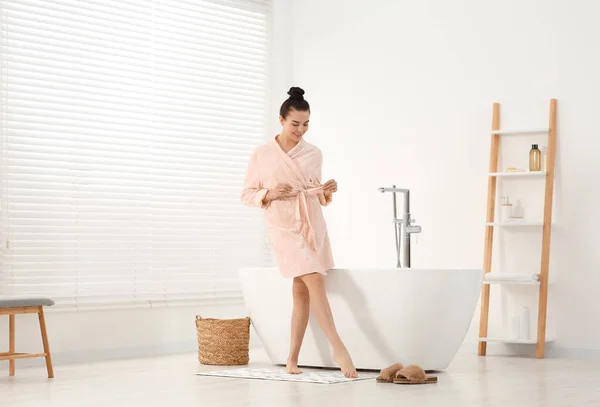 stock image Beautiful happy woman wearing stylish bathrobe near tub in bathroom