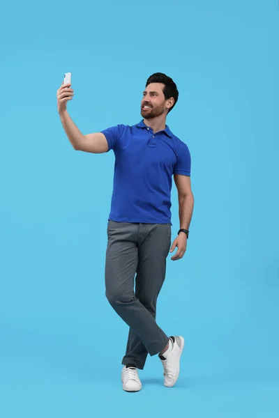 Uśmiechnięty Mężczyzna Robi Selfie Smartfonem Jasnoniebieskim Tle — Zdjęcie stockowe