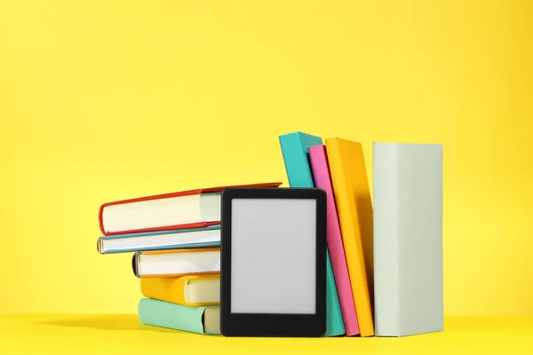 Modern e-book reader and hard cover books on yellow background