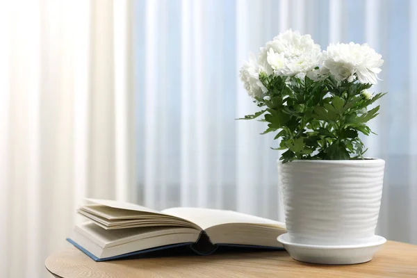 stock image Beautiful chrysanthemum flowers in pot and book on wooden table indoors