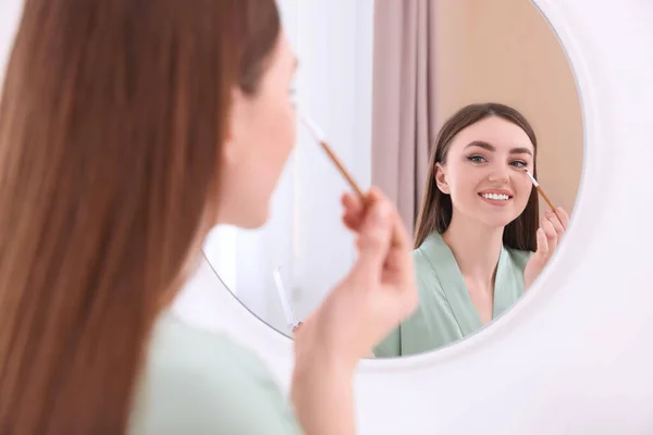 美丽的年轻女子在室内用刷子在镜子前擦眼罩 — 图库照片