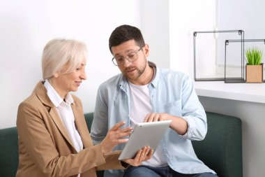 Tabletli ve çalışanı olan mutlu patron koltukta iş meselelerini tartışıyor.