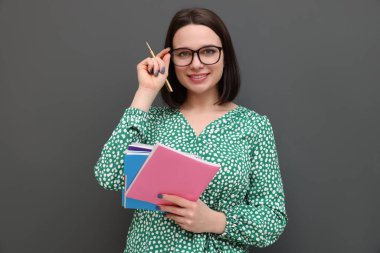 Gri arka planda defterleri ve kalemi olan mutlu bir stajyer.