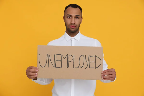 拿着写有 黄色背景失业 字样的标志的年轻人 — 图库照片