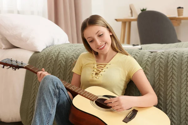 stock image Teenage girl playing acoustic guitar near bed in room