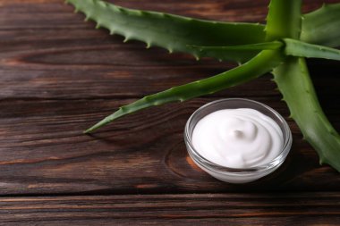 Bir kase kozmetik krem ve aloe vera yaprakları ahşap masada, yakın plan. Metin için boşluk