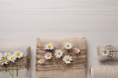 Çuval bezine doldurulmuş hediyeler güzel papatyalar, ipler ve iplerle beyaz ahşap masa üzerinde düz yatıyordu. Metin için boşluk