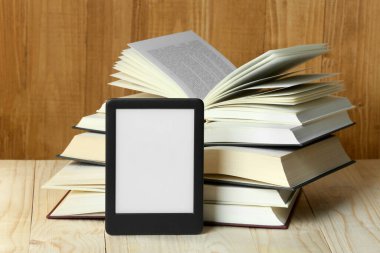 Taşınabilir e-kitap okuyucu ve ahşap masadaki ciltli kitapları aç
