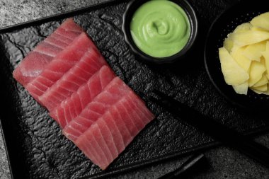 Lezzetli sashimi (taze çiğ ton balığı parçaları) wasabi sosu ve siyah tabakta zencefil dilimleri ile servis edilir.