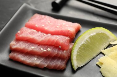 Lezzetli sashimi (taze çiğ ton balığı parçaları) ve siyah tabakta limon dilimi, yakın plan.