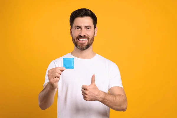 黄色の背景に親指を示すコンドームを持つ幸せな男 安全なセックス — ストック写真
