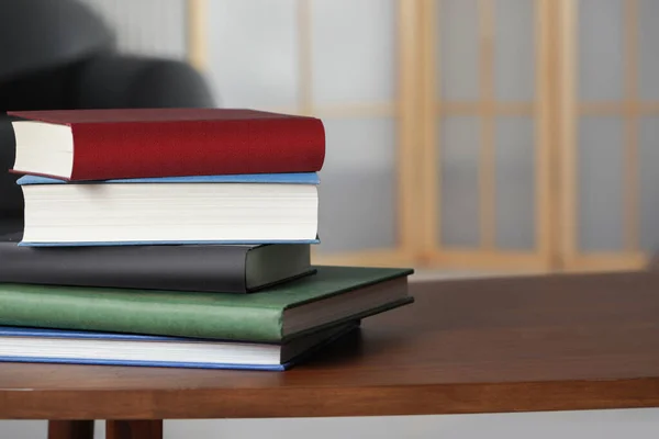 Stack of hardcover books on wooden coffee table indoors, space for text