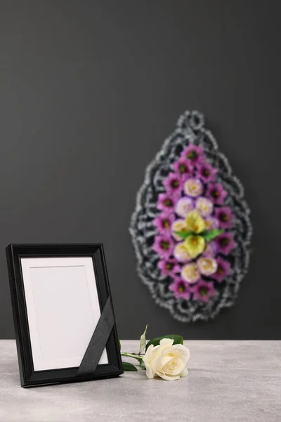 黒いリボンで写真フレームは 屋内の灰色の壁 テキストのためのスペースの近くの花の光のテーブルと花輪に上昇した 葬儀の属性 — ストック写真