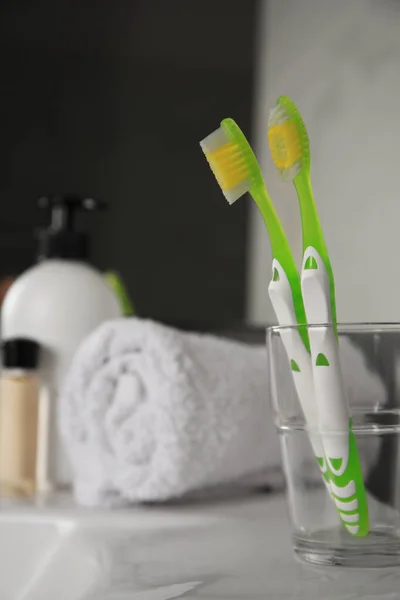 Light green toothbrushes in glass holder on washbasin indoors