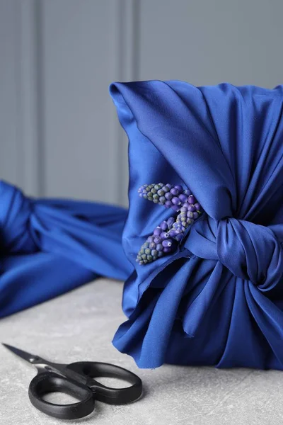 stock image Furoshiki technique. Gift packed in blue silk fabric, muscari flowers and scissors on light grey table