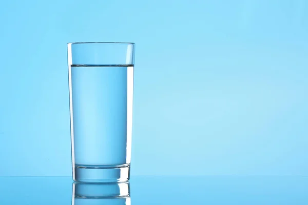 Glass of water on light blue background. Space for text