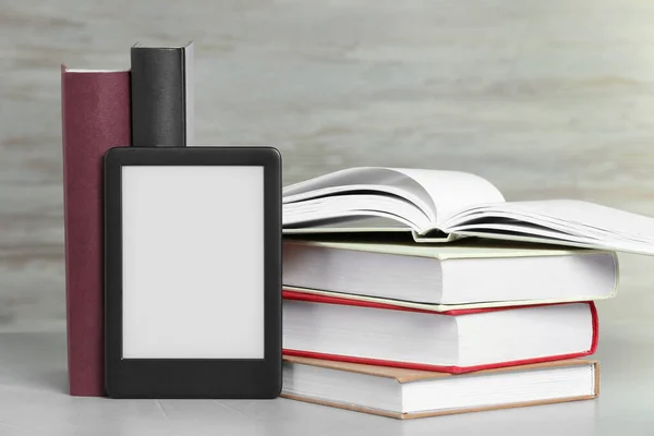 Portable e-book reader and many hardcover books on white textured table
