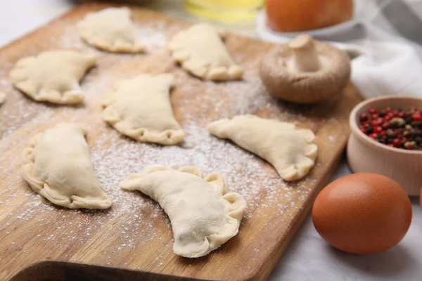 stock image Raw dumplings (varenyky) with tasty filling on wooden board, closeup. Traditional Ukrainian dish