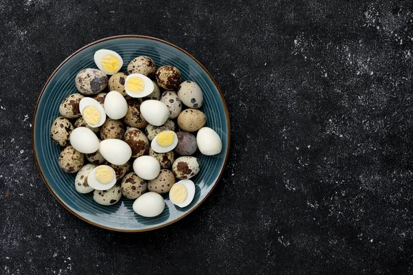 stock image Peeled and unpeeled hard boiled quail eggs in plate on black table, top view. Space for text