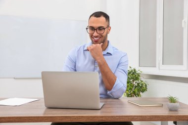 Modern ofiste dizüstü bilgisayarla çalışan genç ve mutlu bir stajyer.